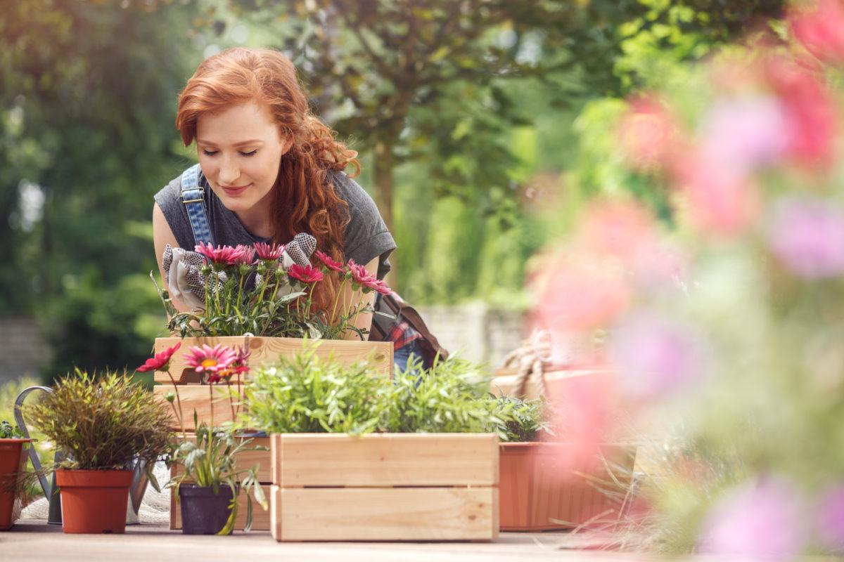 Woman with red hair in her garden, pausing to smell some flowers
