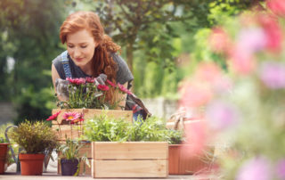 Woman with red hair in her garden, pausing to smell some flowers