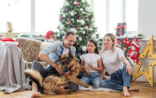 Friendly family is playing with dog near Christmas tree. They are sitting and laughing
